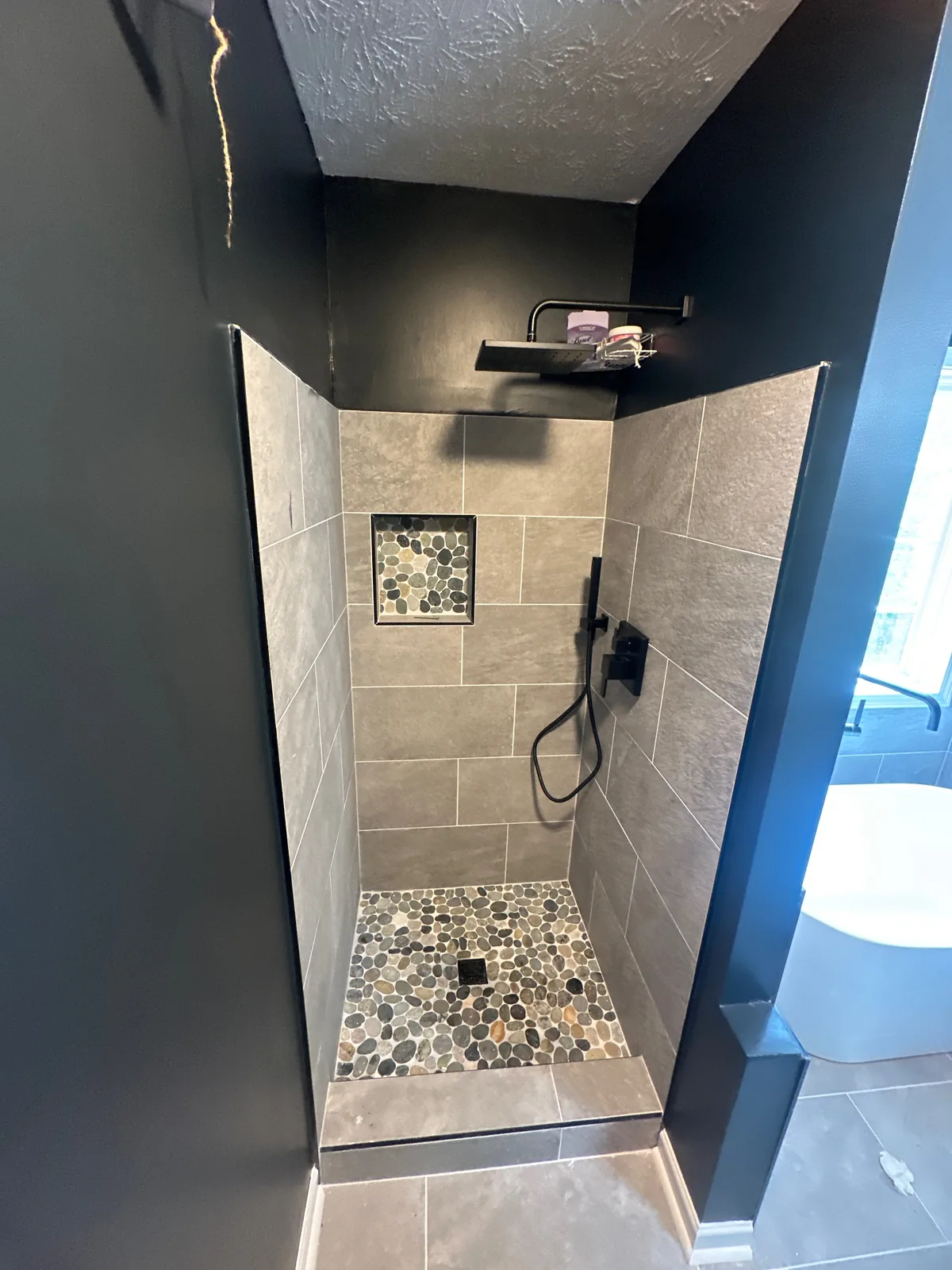 The finished walk-in shower with a pebble floor and tiled niche